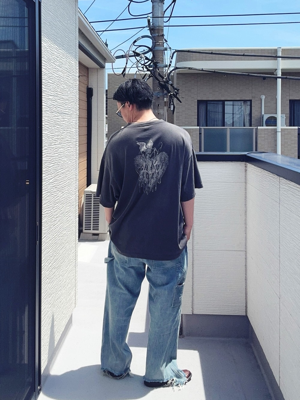 ブルー系のデニムパンツ、ブラック系のTシャツ/カットソー、ブラウン系のローファーを着用したメンズの夏コーディネートの3枚目の写真