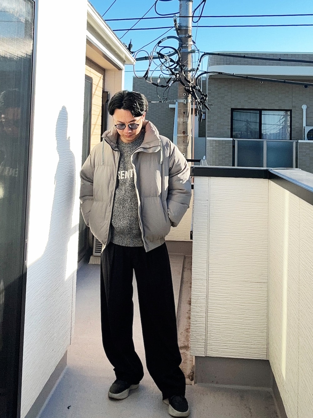 グレー系のニット/セーター、グレー系のダウンジャケット/コート、ブラック系のスラックスを着用したメンズの冬コーディネートの2枚目の写真