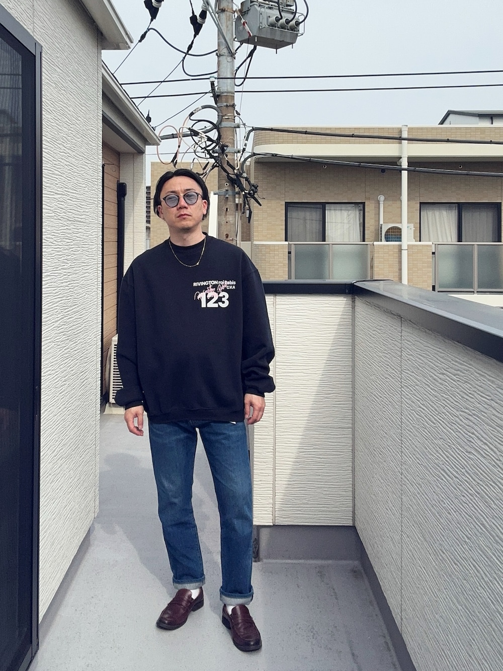 ブルー系のデニムパンツ、ブラック系のスウェット、ブラウン系のローファーを着用したメンズの春コーディネートの2枚目の写真