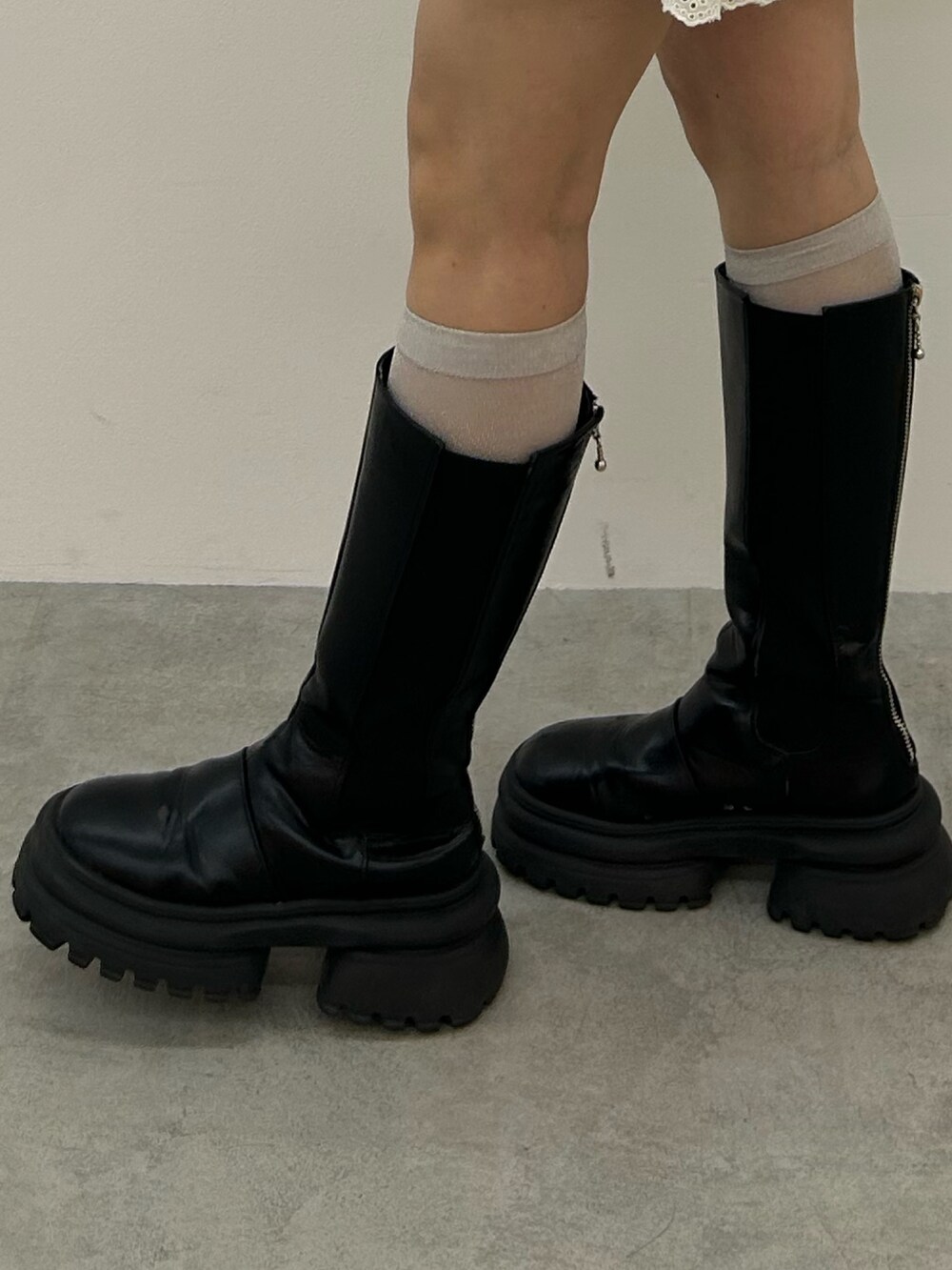 グレー系のワンピース、ブラック系のブーツ、ブルー系のチョーカーを着用したレディースの冬コーディネートの6枚目の写真