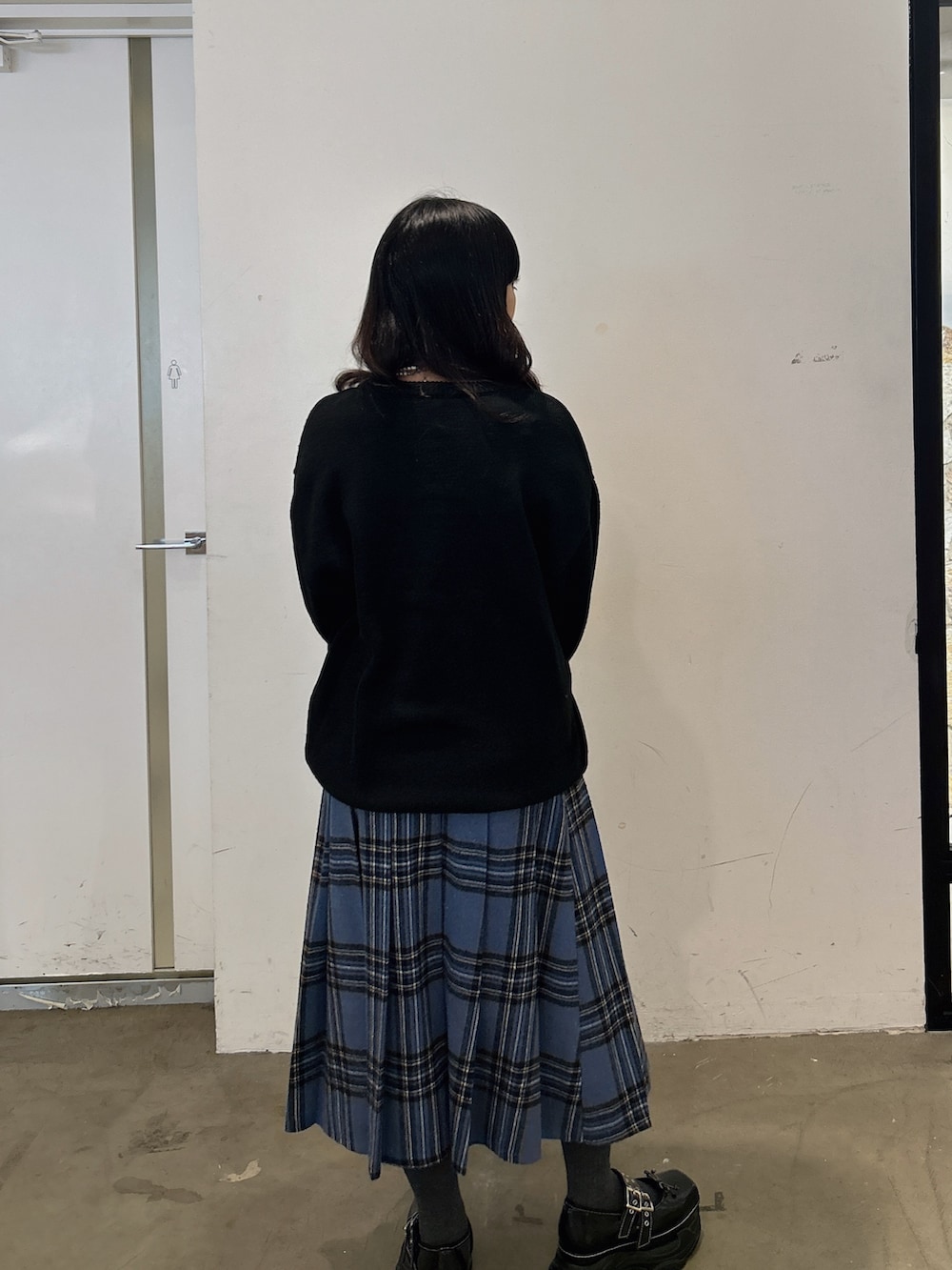 ブラック系のニット/セーター、ブルー系のスカート、ブラック系のスニーカーを着用したレディースの秋コーディネートの3枚目の写真