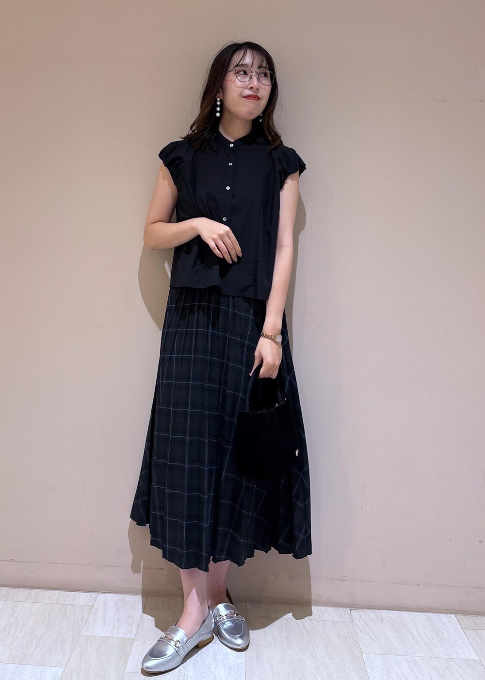 グリーン系のスカート、ブラック系のシャツ/ブラウス、シルバー系のローファーを着用したレディースの夏コーディネートの2枚目の写真