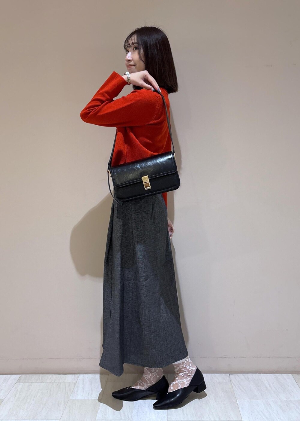 ブラック系のショルダーバッグ、グレー系のスカート、ブラック系のパンプスを着用したレディースの秋コーディネートの2枚目の写真