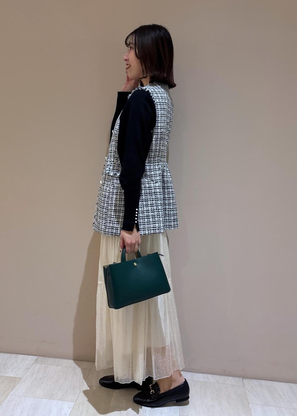 ホワイト系のスカート、グリーン系のショルダーバッグ、ブラック系のニット/セーターを着用したレディースの冬コーディネートの2枚目の写真