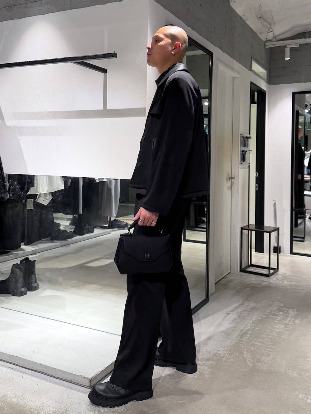 ブラック系のスラックス、ブラック系のハンドバッグ、ブラック系のドレスシューズを着用したメンズの春コーディネートの2枚目の写真