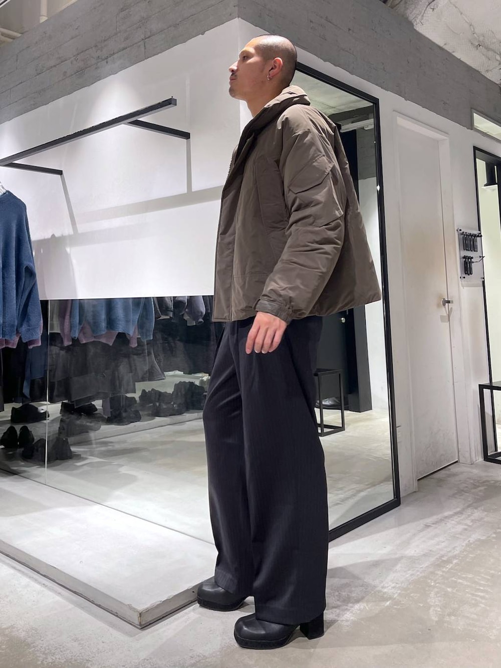 イエロー系のニット/セーター、ブラック系のトートバッグ、ブラウン系のダウンジャケット/コートを着用したメンズの冬コーディネートの2枚目の写真