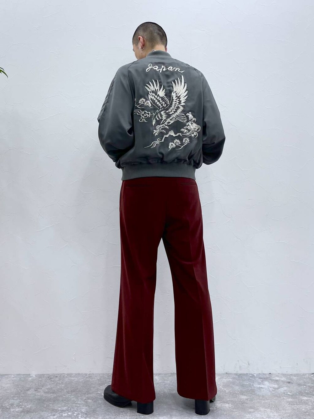 グレー系のスカジャン、ブラック系のブーツ、レッド系のスラックスを着用したメンズの秋コーディネートの2枚目の写真