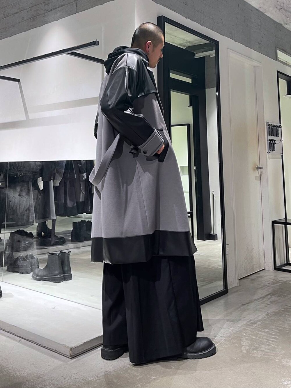 グレー系のトレンチコート、ブラック系のブーツ、ブラック系のスラックスを着用したメンズの秋コーディネートの4枚目の写真