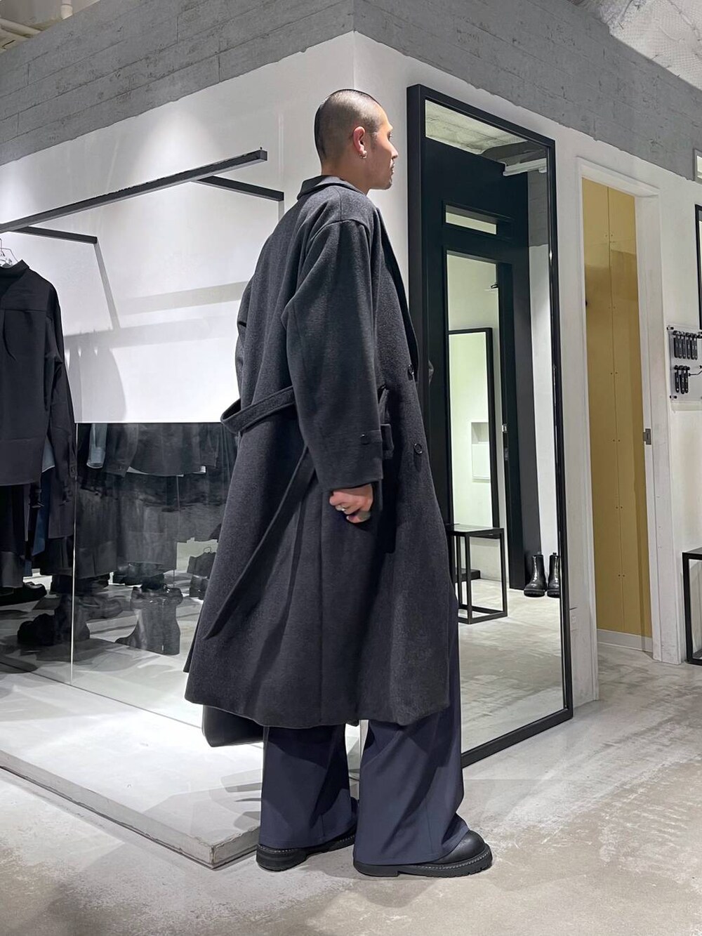 グレー系のチェスターコート、ブラック系のトートバッグ、ブラック系のブーツを着用したメンズの冬コーディネートの4枚目の写真