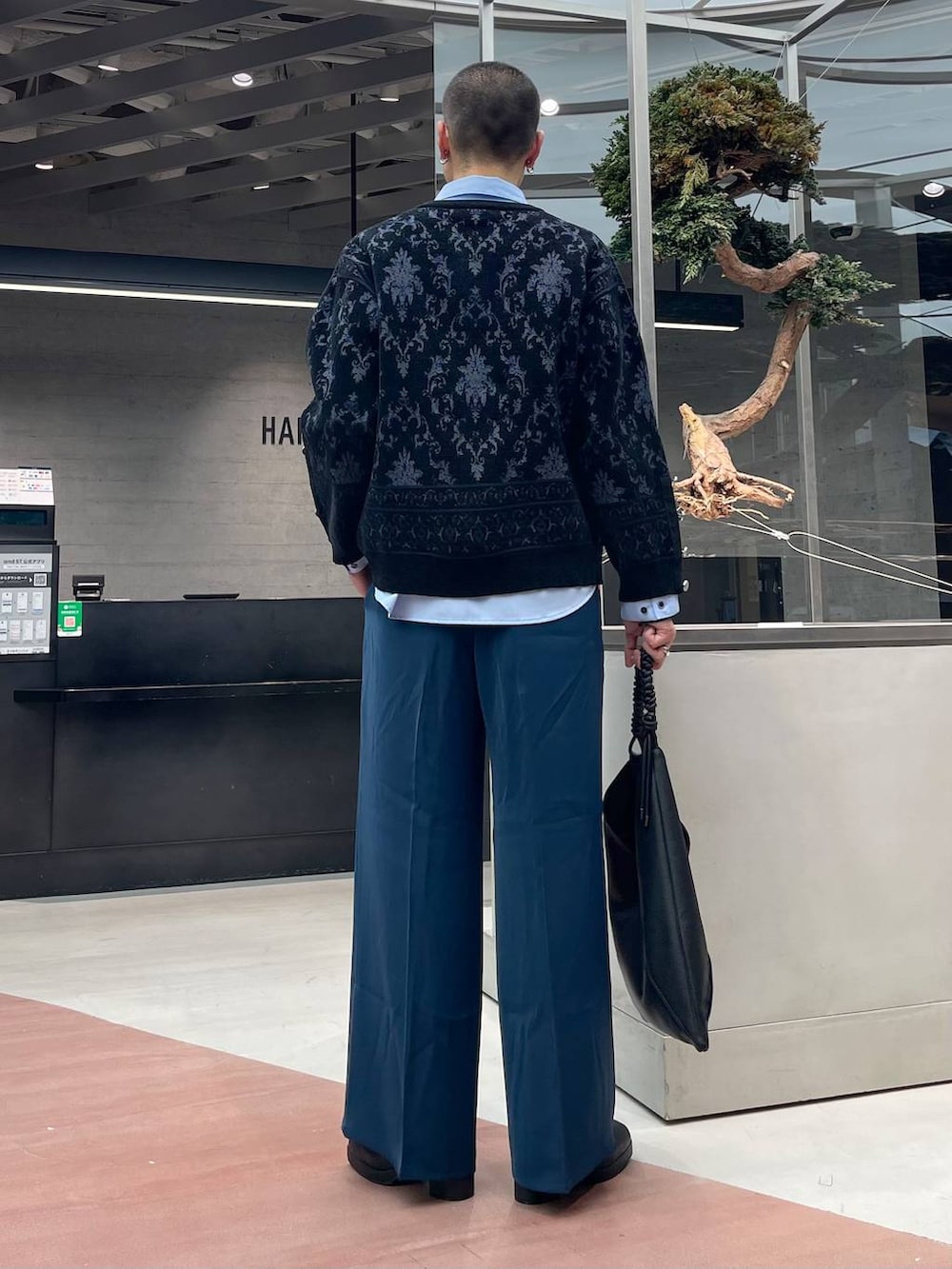 ブルー系のスラックス、ブラック系のカーディガン/ボレロ、ブラック系のトートバッグを着用したメンズの秋コーディネートの3枚目の写真