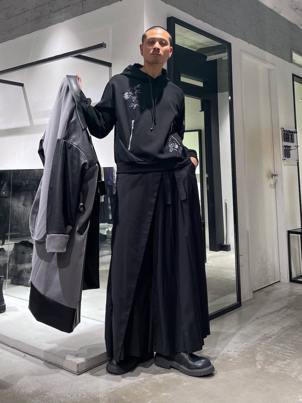 グレー系のトレンチコート、ブラック系のブーツ、ブラック系のスラックスを着用したメンズの秋コーディネートの5枚目の写真