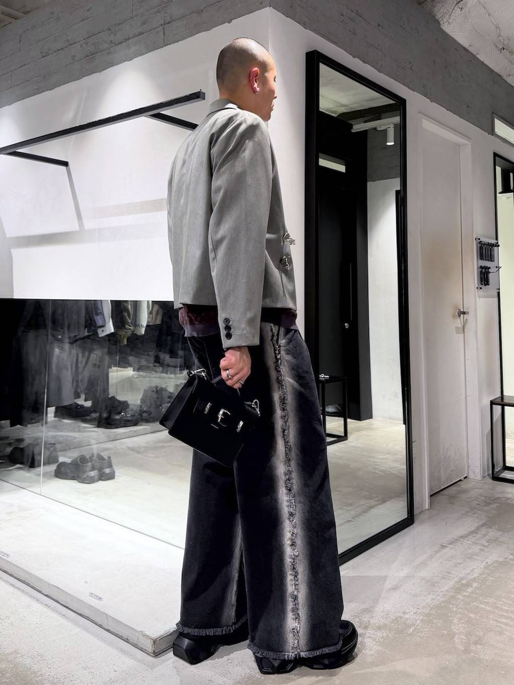 ブラック系のスニーカー、ブラック系のハンドバッグ、ブラック系のデニムパンツを着用したメンズの冬コーディネートの4枚目の写真