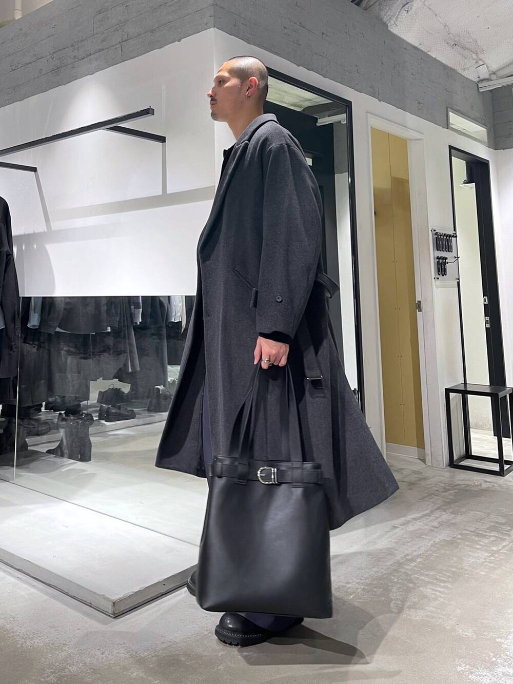 グレー系のチェスターコート、ブラック系のトートバッグ、ブラック系のブーツを着用したメンズの冬コーディネートの2枚目の写真