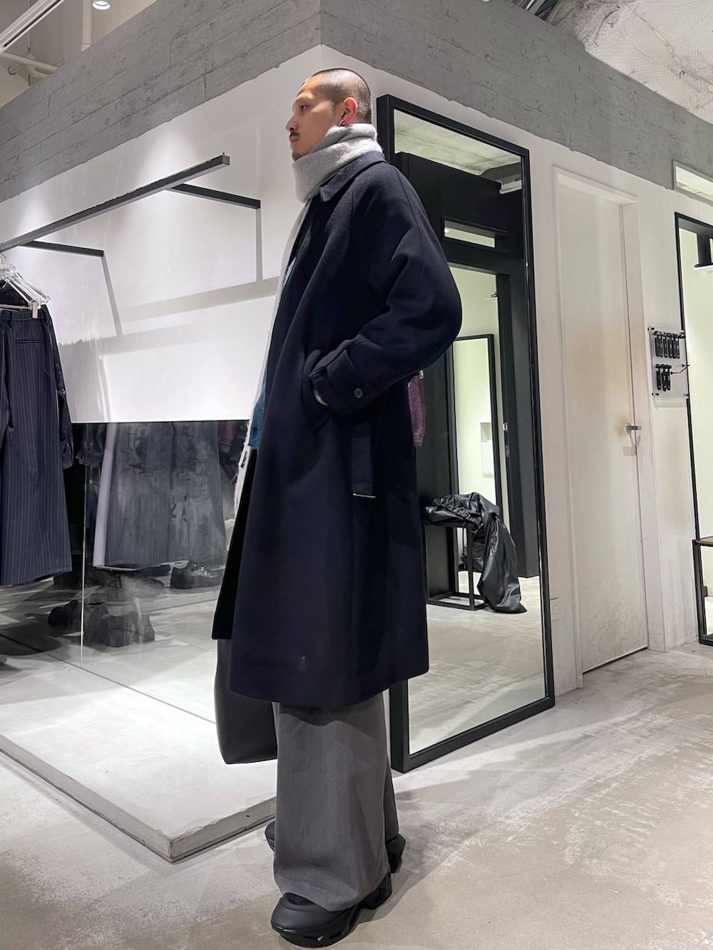ブラック系のステンカラーコート、ブルー系のカーディガン/ボレロ、ブラック系のトートバッグを着用したメンズの冬コーディネートの2枚目の写真