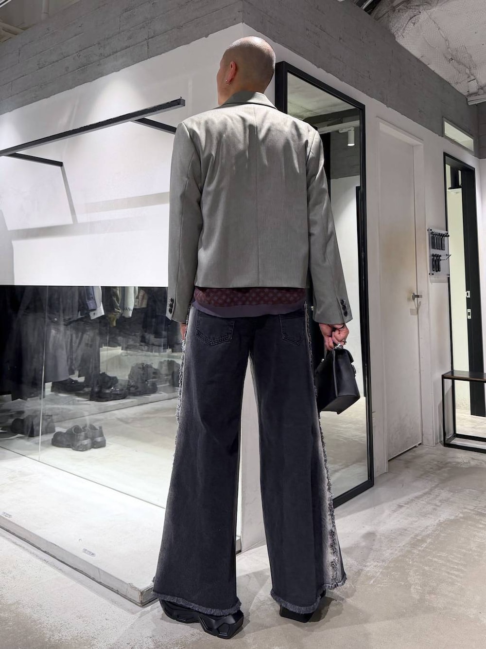 ブラック系のスニーカー、ブラック系のハンドバッグ、ブラック系のデニムパンツを着用したメンズの冬コーディネートの3枚目の写真