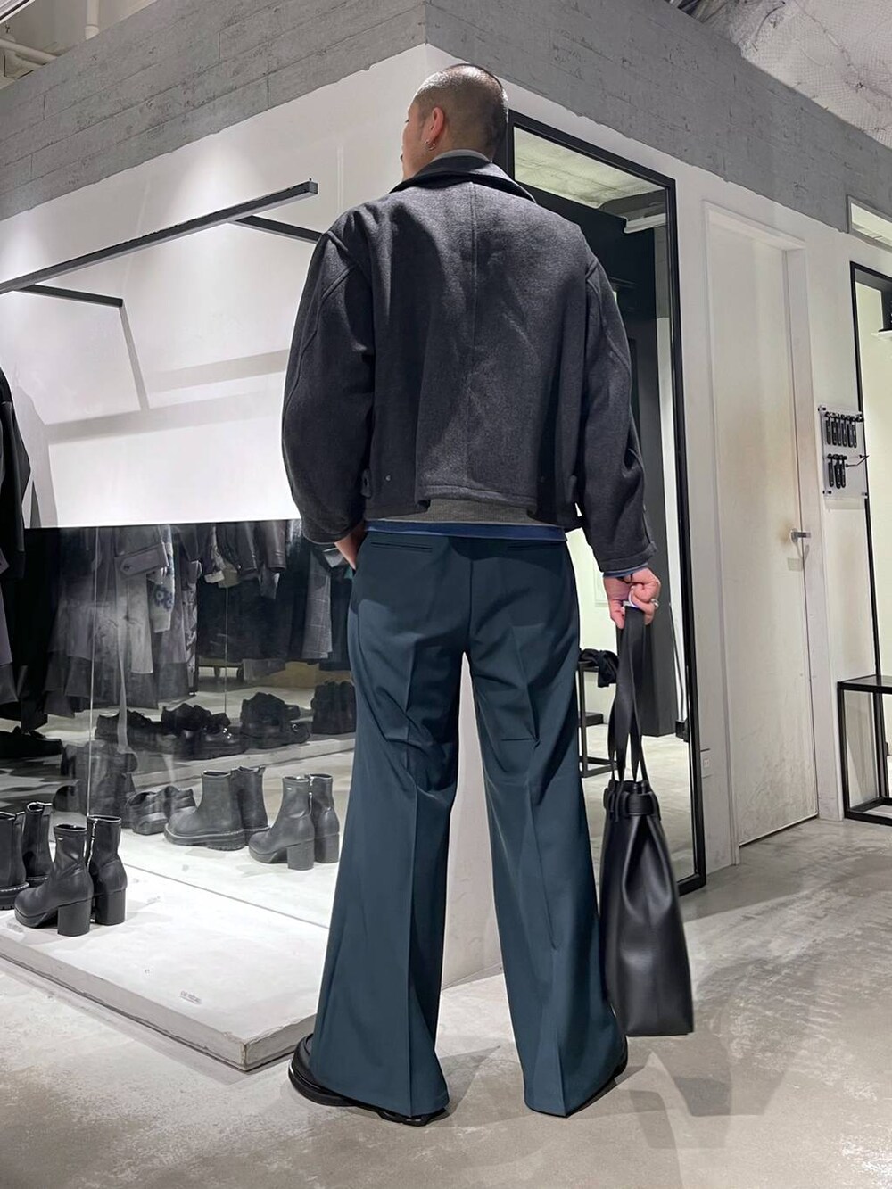 グレー系のブルゾン、ブラック系のトートバッグ、グリーン系のスラックスを着用したメンズの秋コーディネートの3枚目の写真