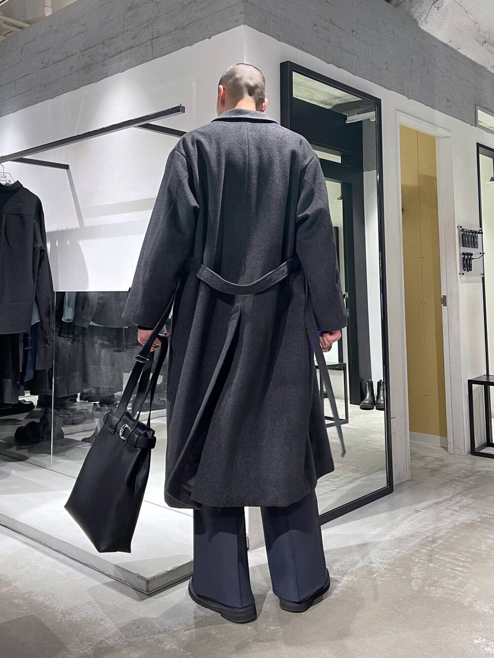 グレー系のチェスターコート、ブラック系のトートバッグ、ブラック系のブーツを着用したメンズの冬コーディネートの3枚目の写真