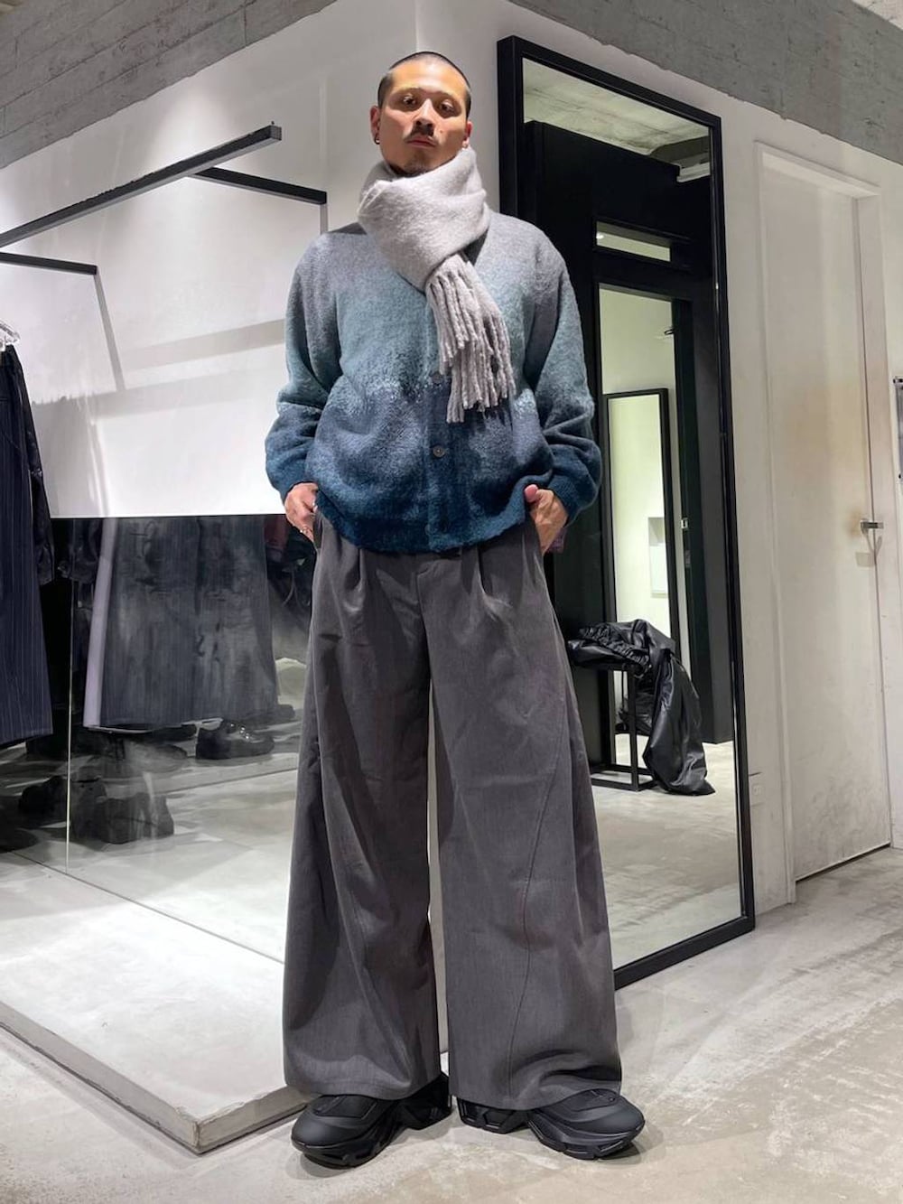 ブラック系のステンカラーコート、ブルー系のカーディガン/ボレロ、ブラック系のトートバッグを着用したメンズの冬コーディネートの5枚目の写真