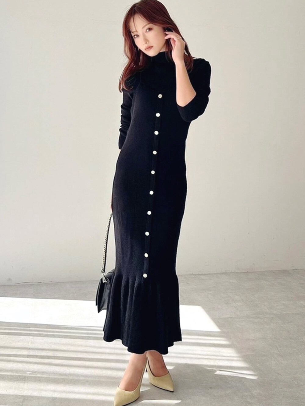 イエロー系のパンプス、ブラック系のワンピース、ブラック系のハンドバッグを着用したレディースの冬コーディネートの2枚目の写真