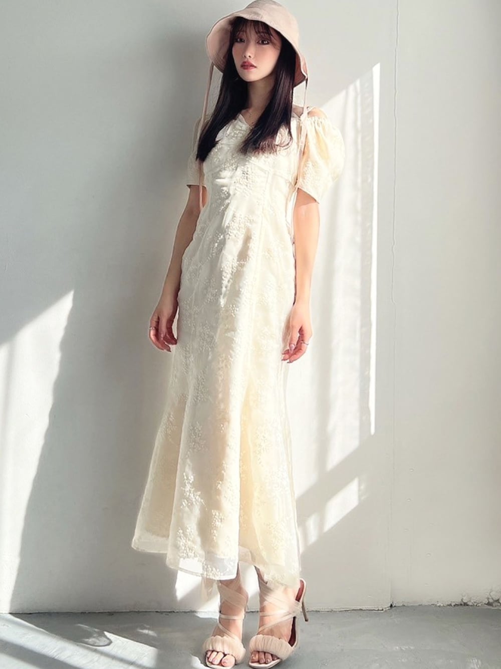 ホワイト系のワンピース、ベージュ系のサンダル、ピンク系のハットを着用したレディースの春コーディネートの2枚目の写真