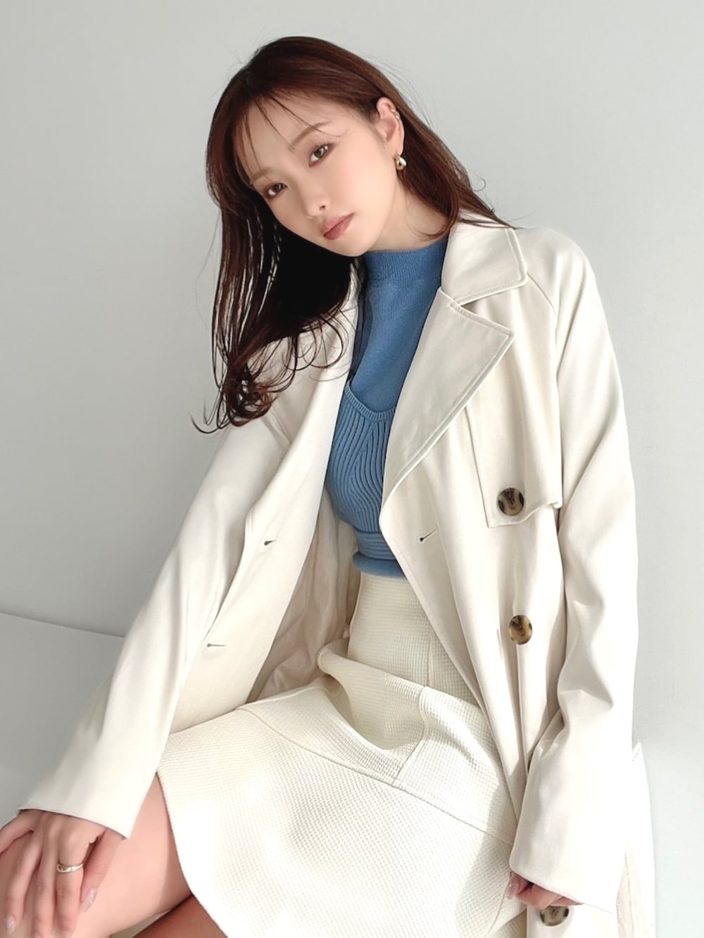 ブルー系のニット/セーター、ホワイト系のトレンチコート、ホワイト系のスカートを着用したレディースの冬コーディネートの2枚目の写真