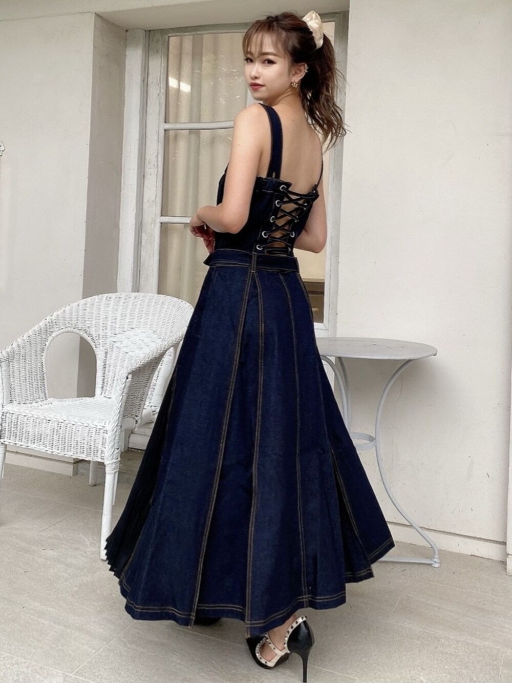 ブラック系のパンプス、ブルー系のジャンパースカート、ピンク系のシュシュを着用したレディースの夏コーディネートの3枚目の写真