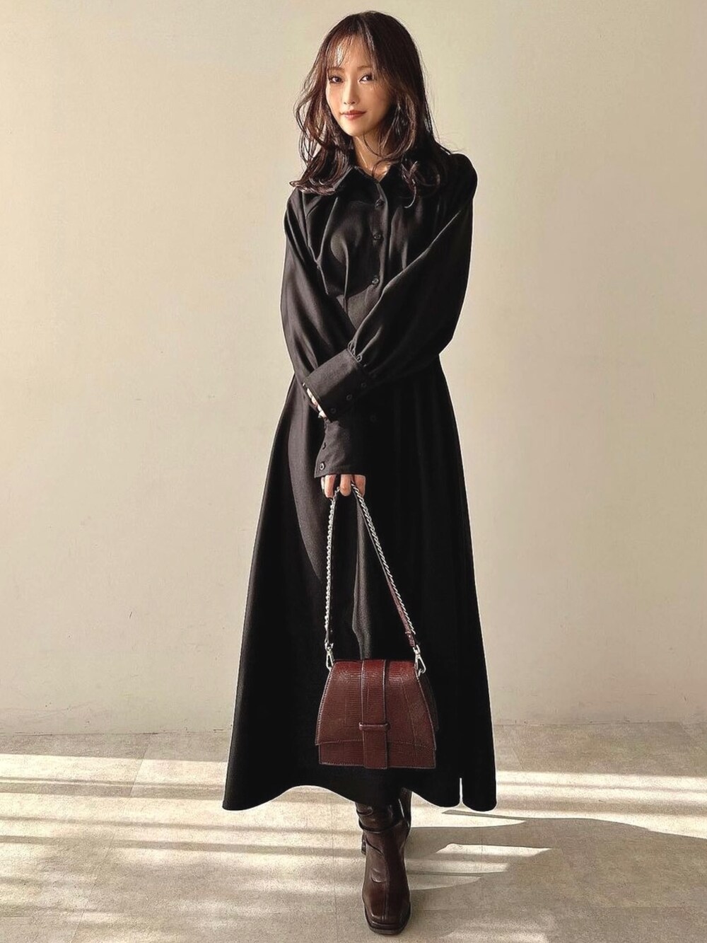 ブラック系のワンピース、ブラウン系のハンドバッグ、ブラウン系のブーツを着用したレディースの冬コーディネートの2枚目の写真