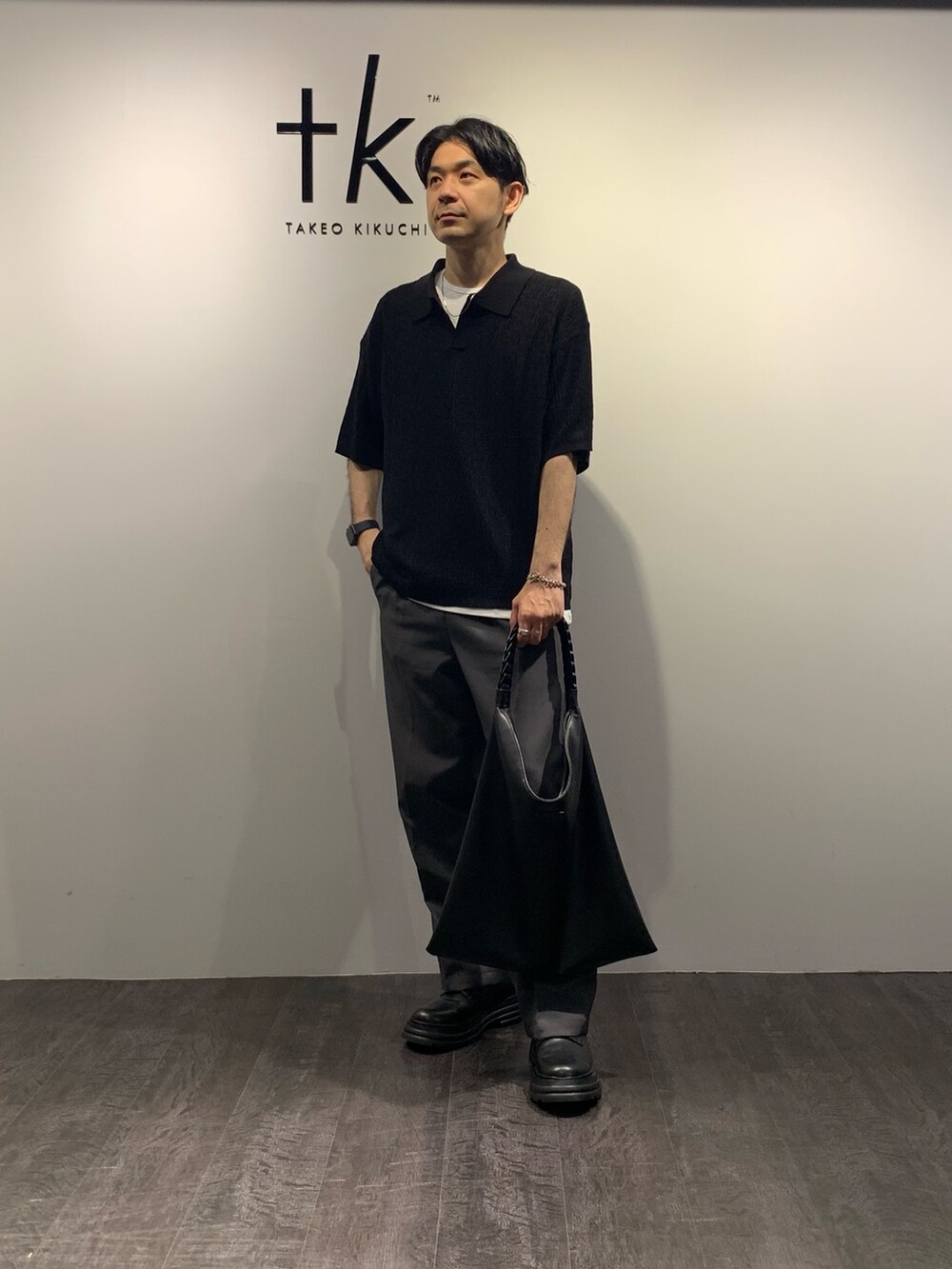 ブラック系のポロシャツ、ブラック系のトートバッグ、ホワイト系のTシャツ/カットソーを着用したメンズの夏コーディネートの2枚目の写真