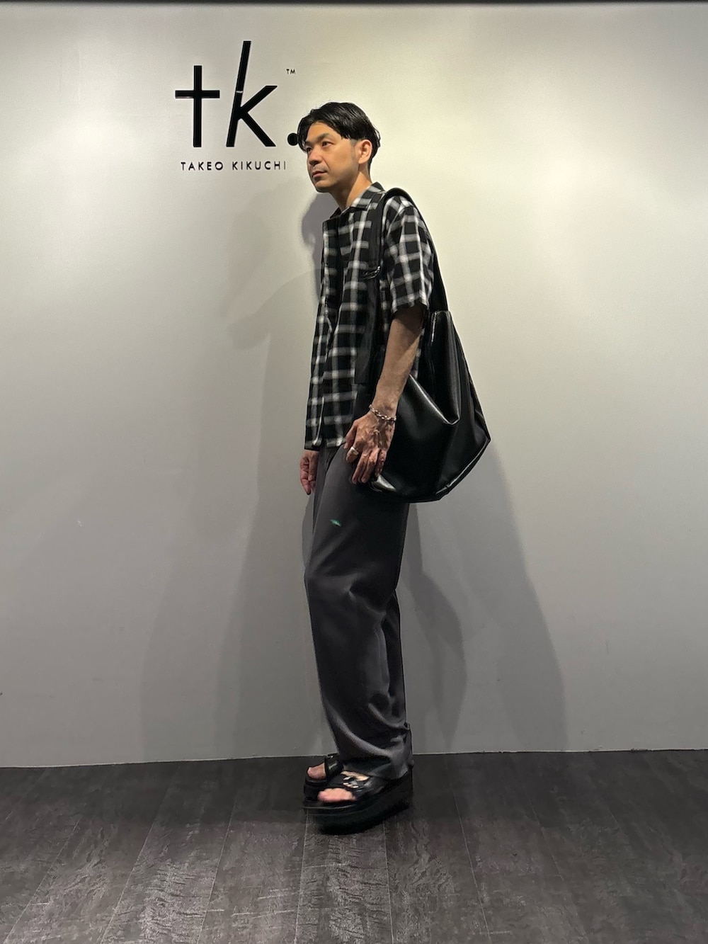 グレー系のスラックス、ブラック系のサンダル、ブラック系のTシャツ/カットソーを着用したメンズの夏コーディネートの2枚目の写真