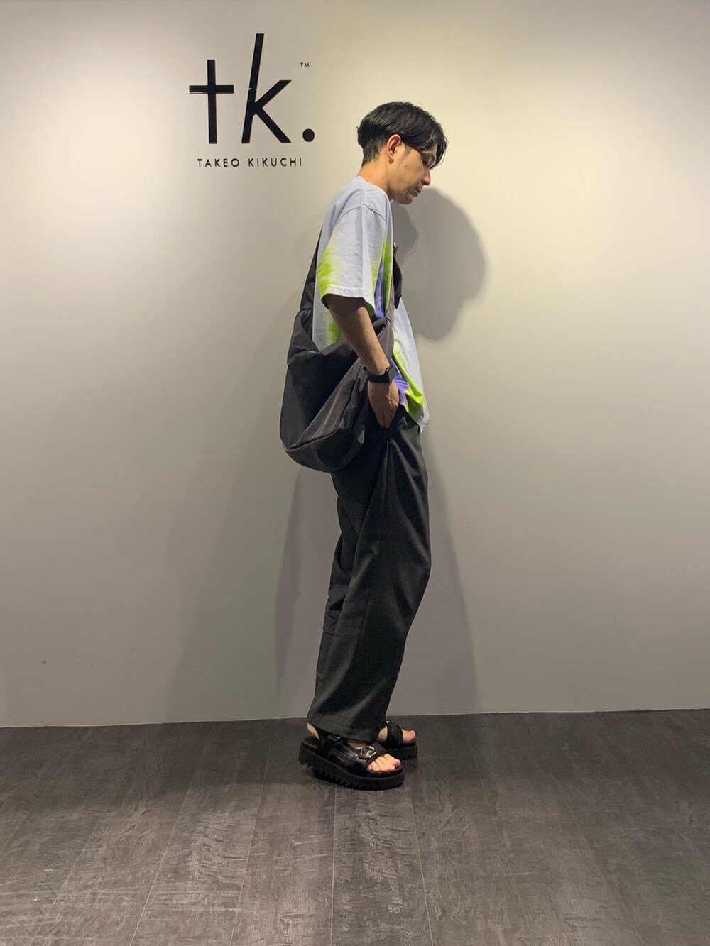 グレー系のスラックス、ブラック系のサンダル、ブルー系のTシャツ/カットソーを着用したメンズの夏コーディネートの2枚目の写真