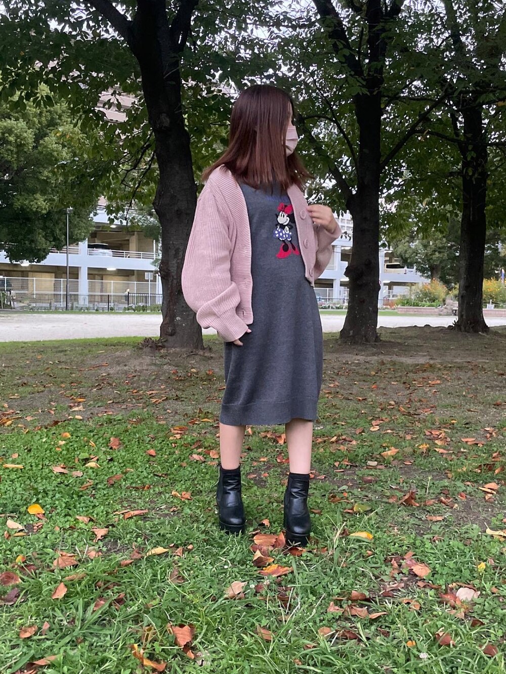 グレー系のワンピース、ピンク系のカーディガン/ボレロ、ブラック系のブーツを着用したレディースの秋コーディネートの2枚目の写真