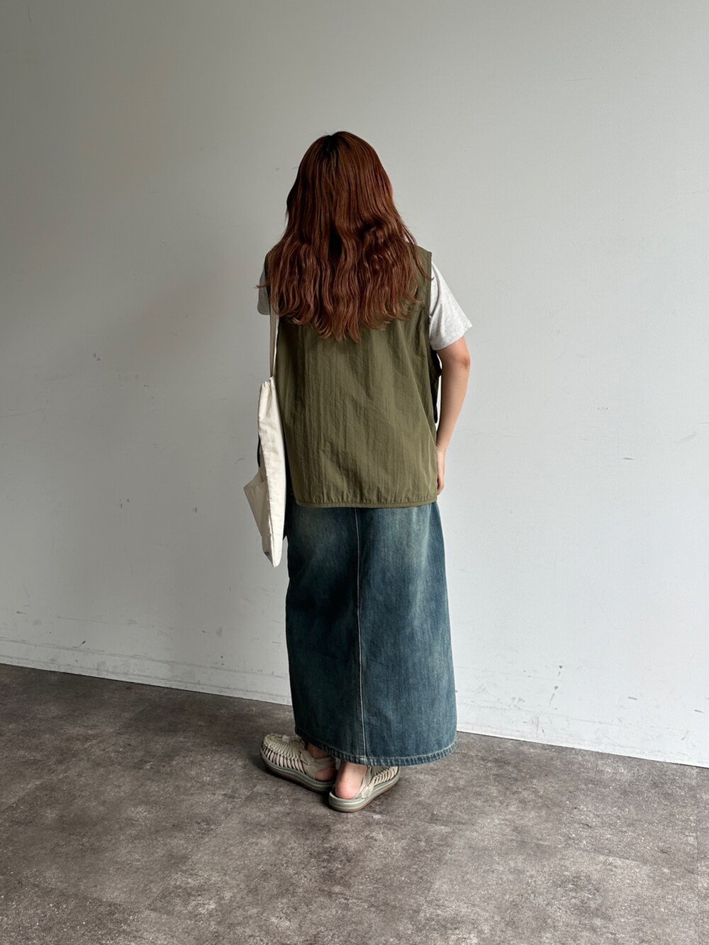 グリーン系のベスト、ブルー系のスカート、ホワイト系のトートバッグを着用したレディースの夏コーディネートの2枚目の写真