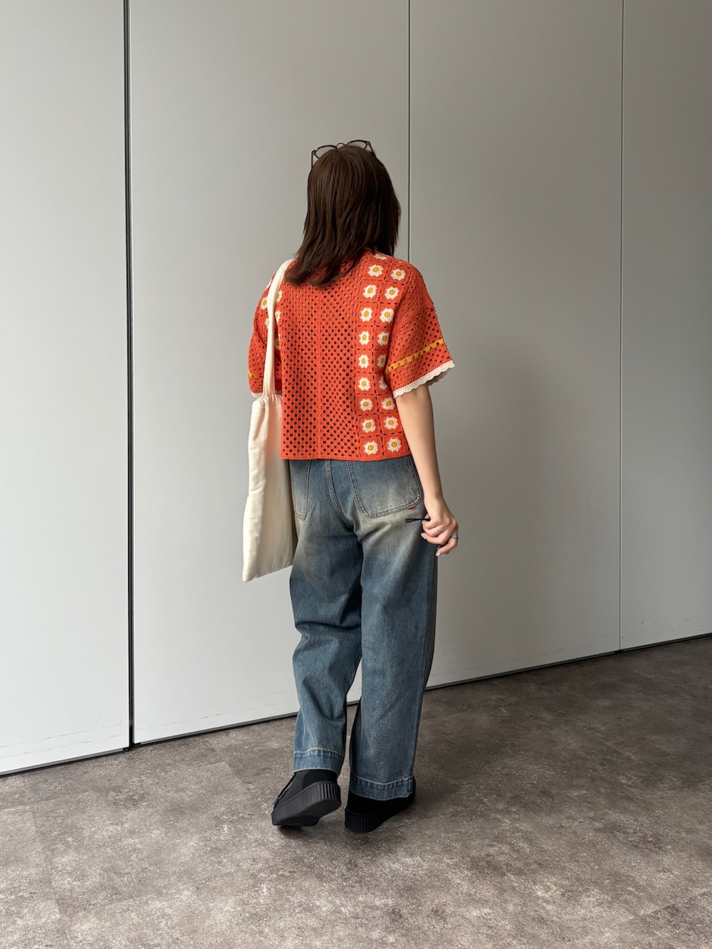 ブルー系のデニムパンツ、オレンジ系のニット/セーター、ホワイト系のトートバッグを着用したレディースの春コーディネートの2枚目の写真