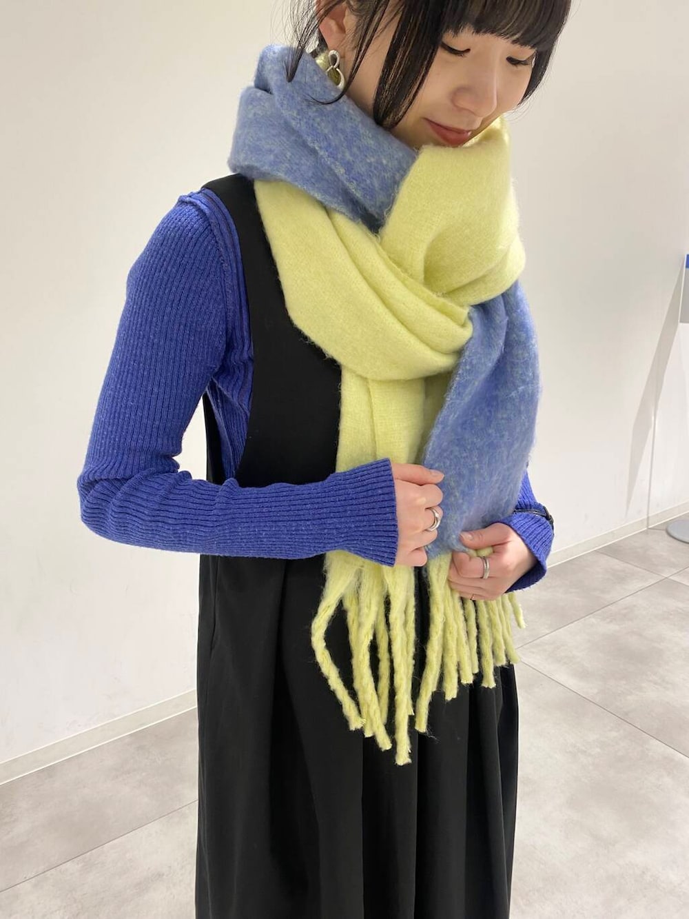 ブラック系のワンピース、ブルー系のニット/セーター、イエロー系のマフラーを着用したレディースの冬コーディネートの2枚目の写真