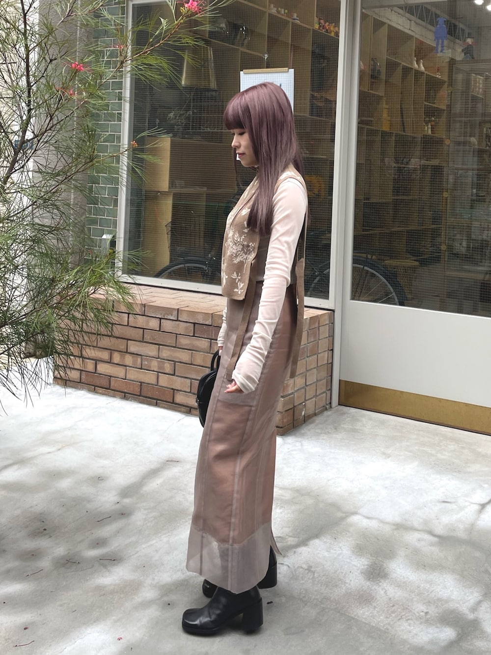 ベージュ系のベスト、ベージュ系のスカート、ブラック系のブーツを着用したレディースの春コーディネートの2枚目の写真