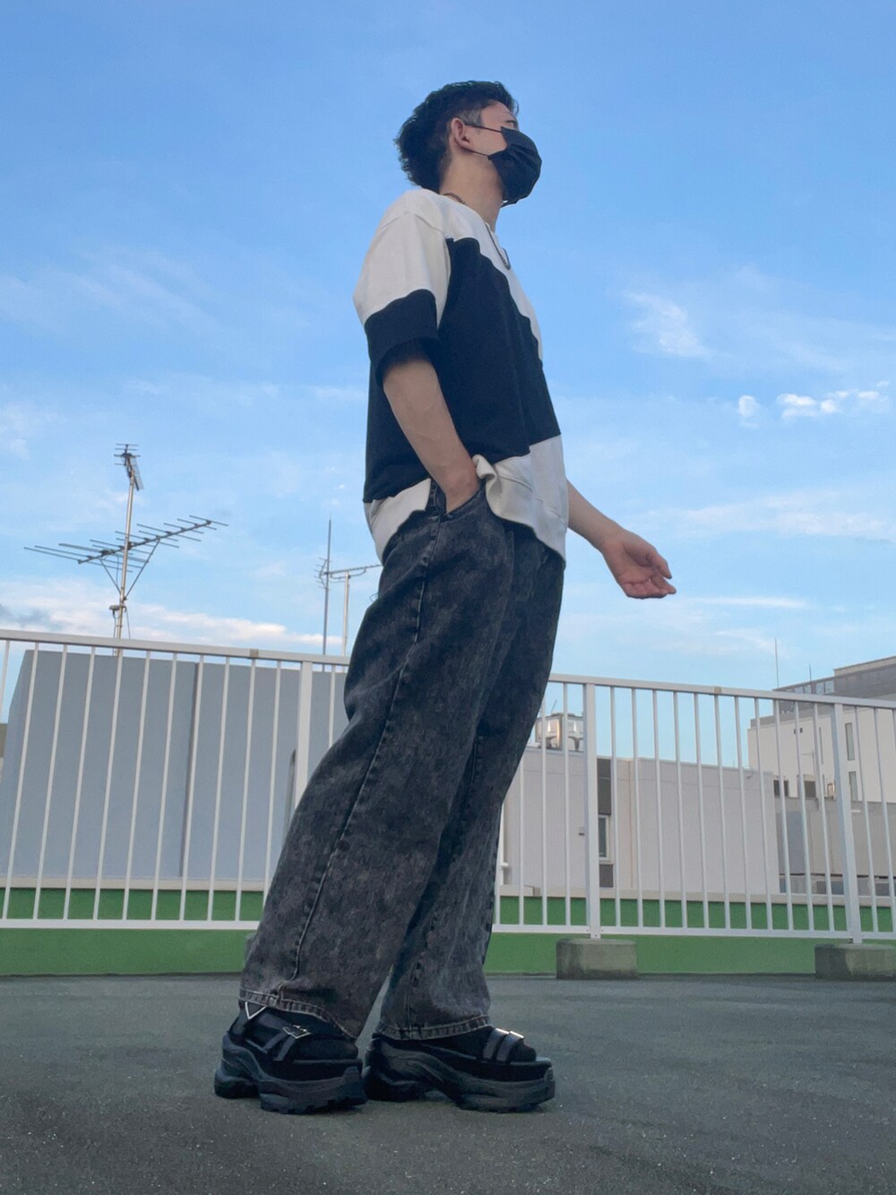 ホワイト系のトップス、ブラック系のデニムパンツ、ブラック系のサンダルを着用したメンズの夏コーディネートの3枚目の写真