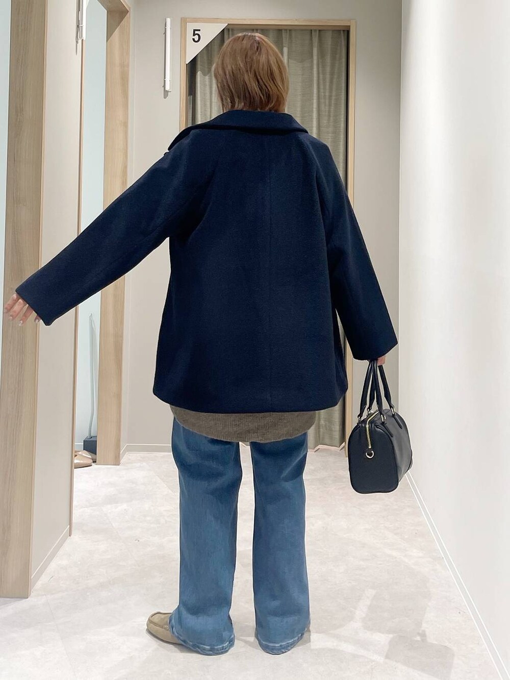 ブルー系のチェスターコート、ブラウン系のニット/セーター、ブラック系のボストンバッグを着用したレディースの秋コーディネートの3枚目の写真