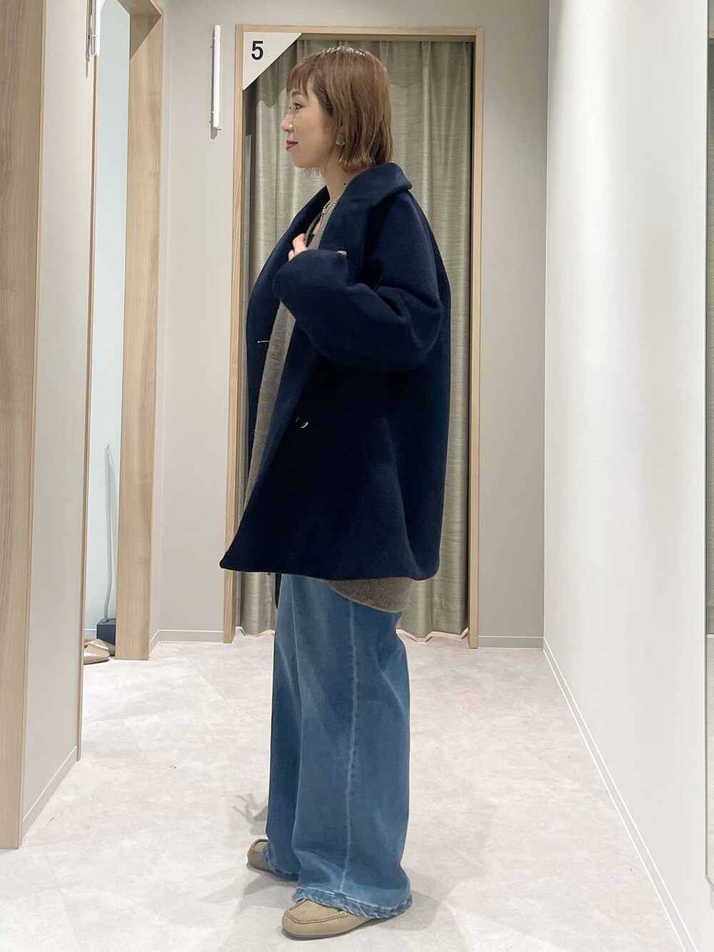 ブルー系のチェスターコート、ブラウン系のニット/セーター、ブラック系のボストンバッグを着用したレディースの秋コーディネートの2枚目の写真