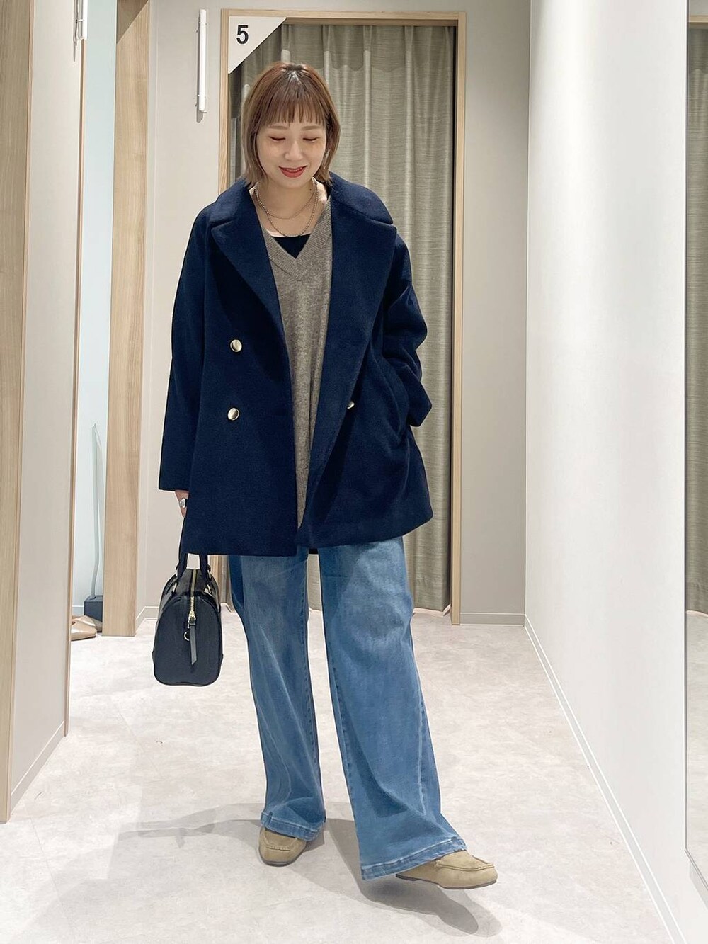 ブルー系のチェスターコート、ブラウン系のニット/セーター、ブラック系のボストンバッグを着用したレディースの秋コーディネートの4枚目の写真