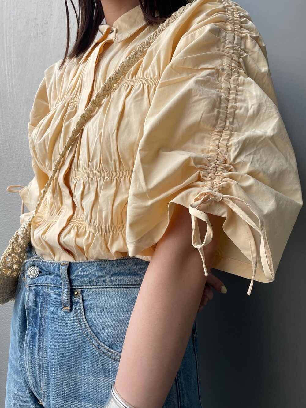 ブルー系のデニムパンツ、イエロー系のシャツ/ブラウス、ベージュ系のショルダーバッグを着用したレディースの春コーディネートの4枚目の写真