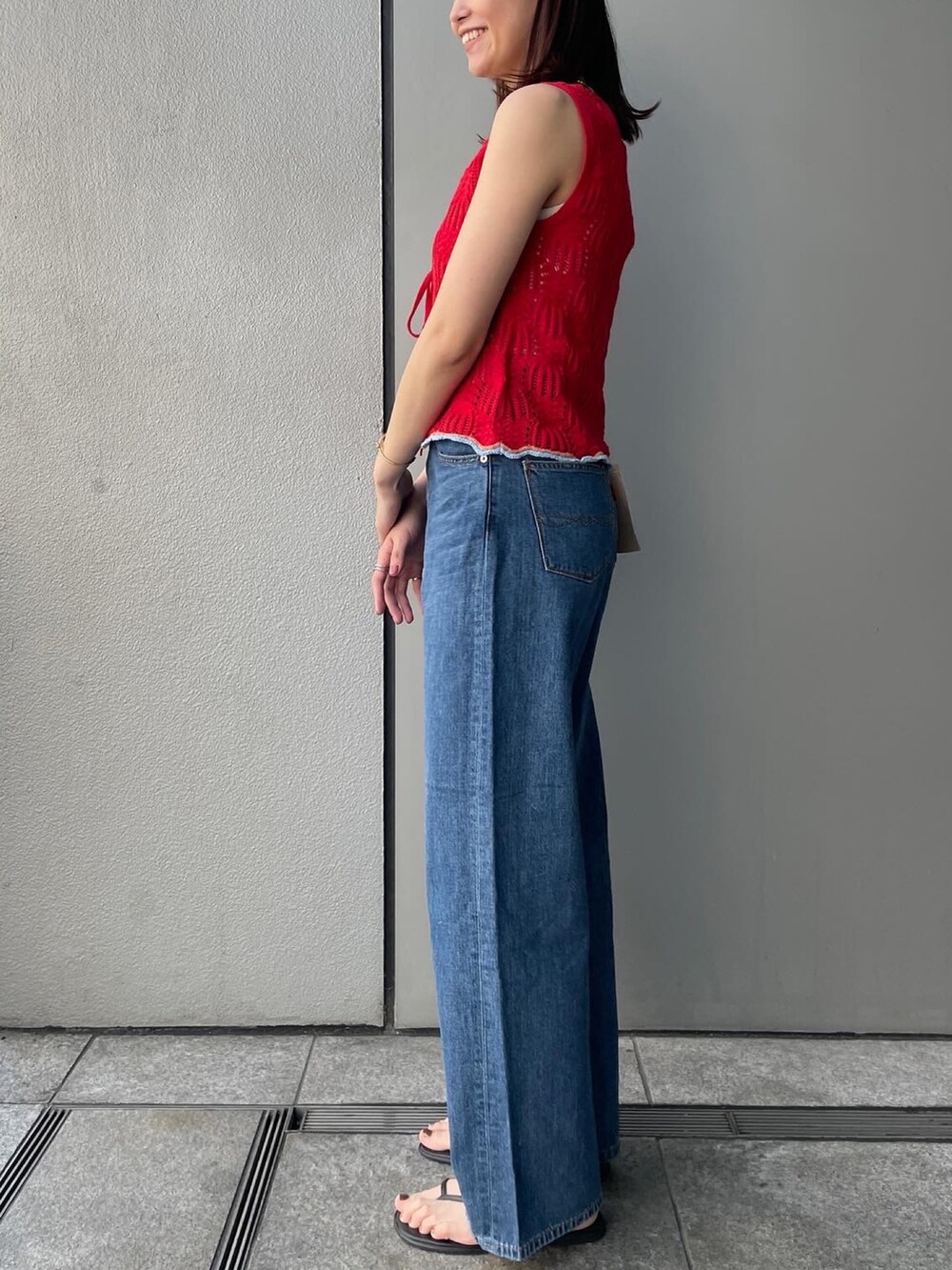 レッド系のニット/セーター、ブルー系のデニムパンツ、ホワイト系のキャミソールを着用したレディースの春コーディネートの3枚目の写真