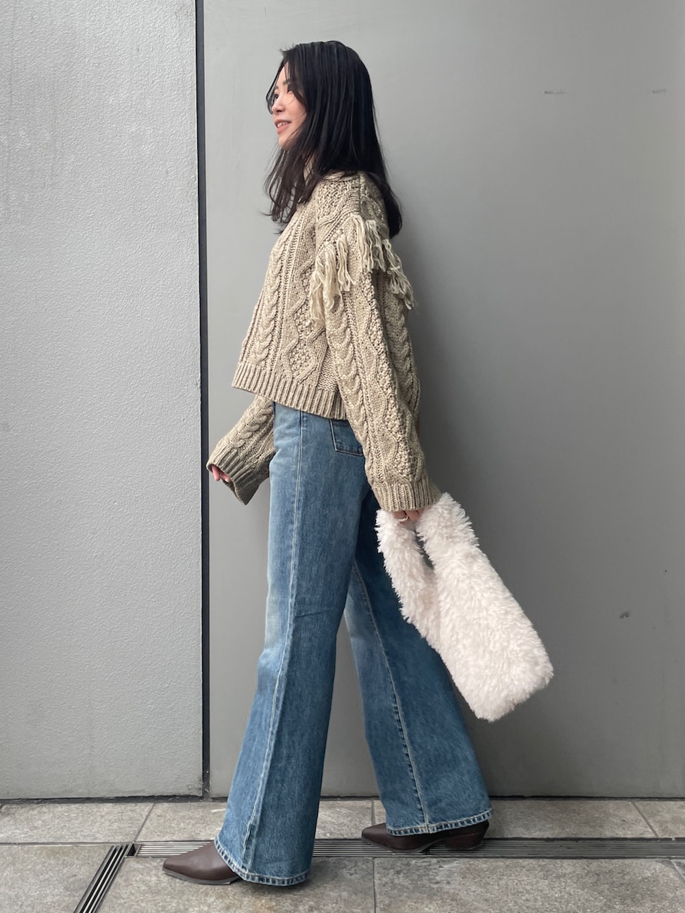 ブルー系のデニムパンツ、ブラウン系のニット/セーター、ホワイト系のハンドバッグを着用したレディースの冬コーディネートの2枚目の写真