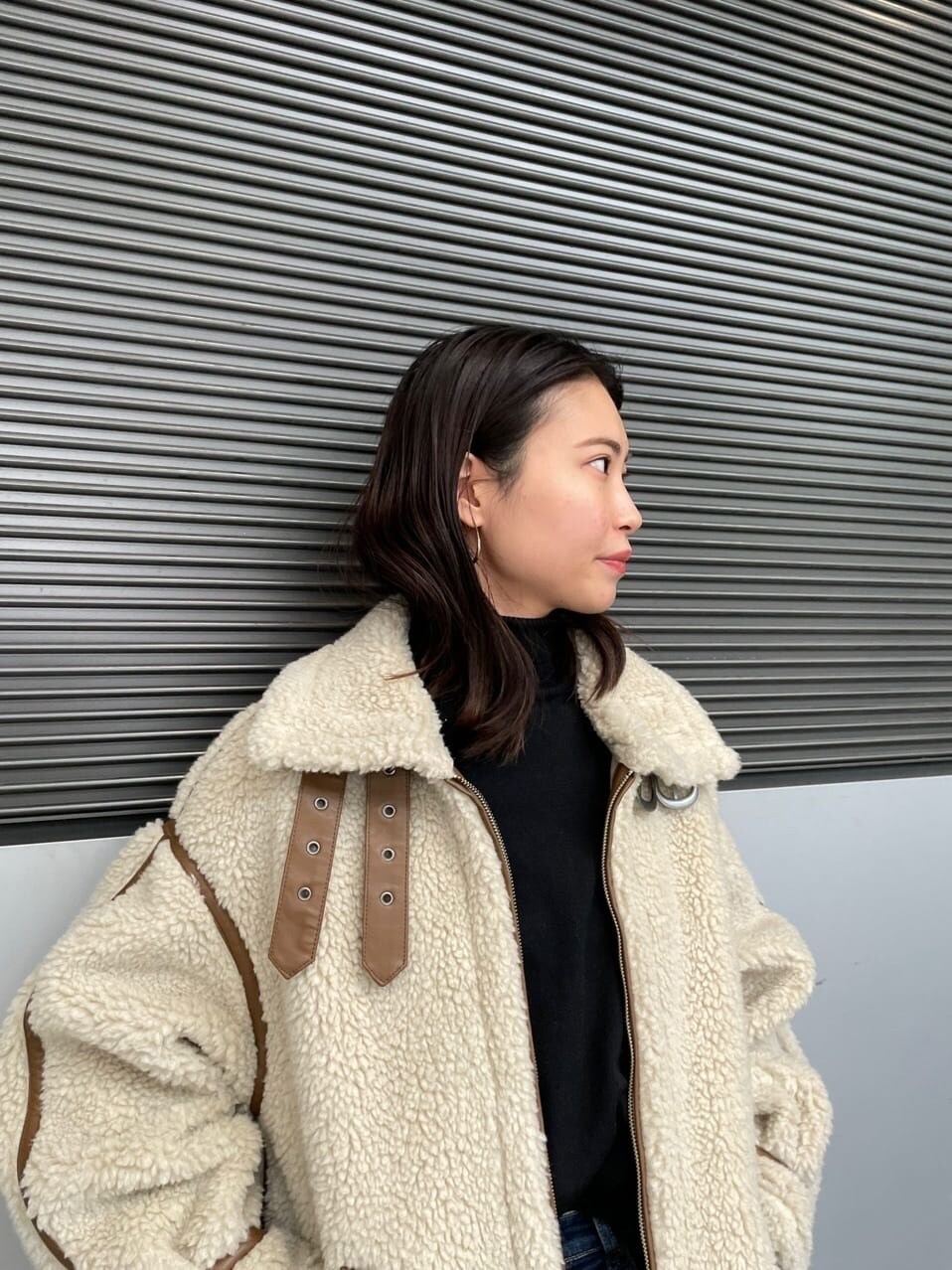 ブラック系のニット/セーター、ホワイト系のムートンコート、ブルー系のデニムパンツを着用したレディースの冬コーディネートの3枚目の写真