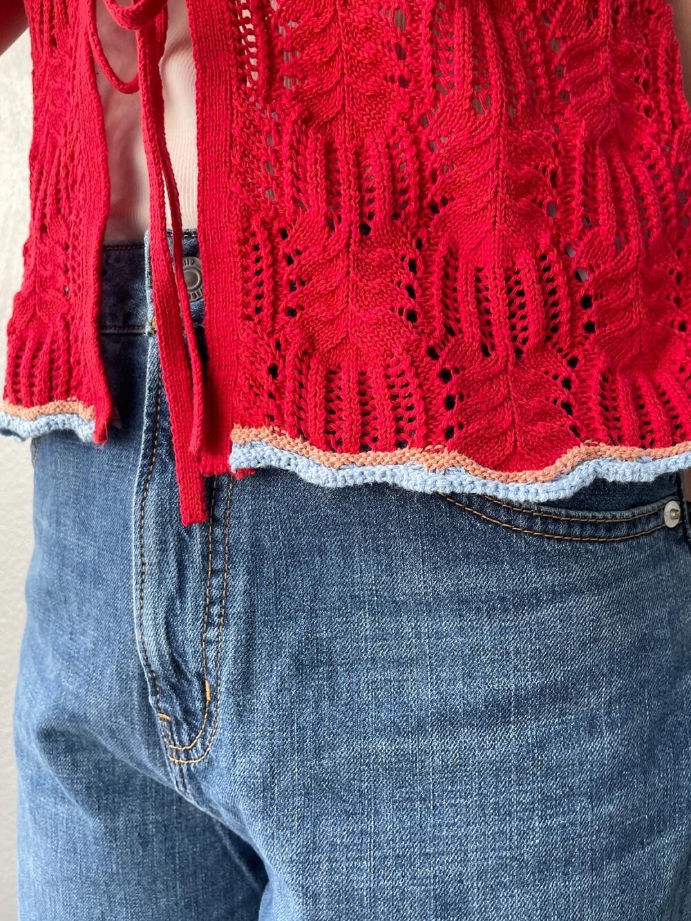 レッド系のニット/セーター、ブルー系のデニムパンツ、ホワイト系のキャミソールを着用したレディースの春コーディネートの4枚目の写真