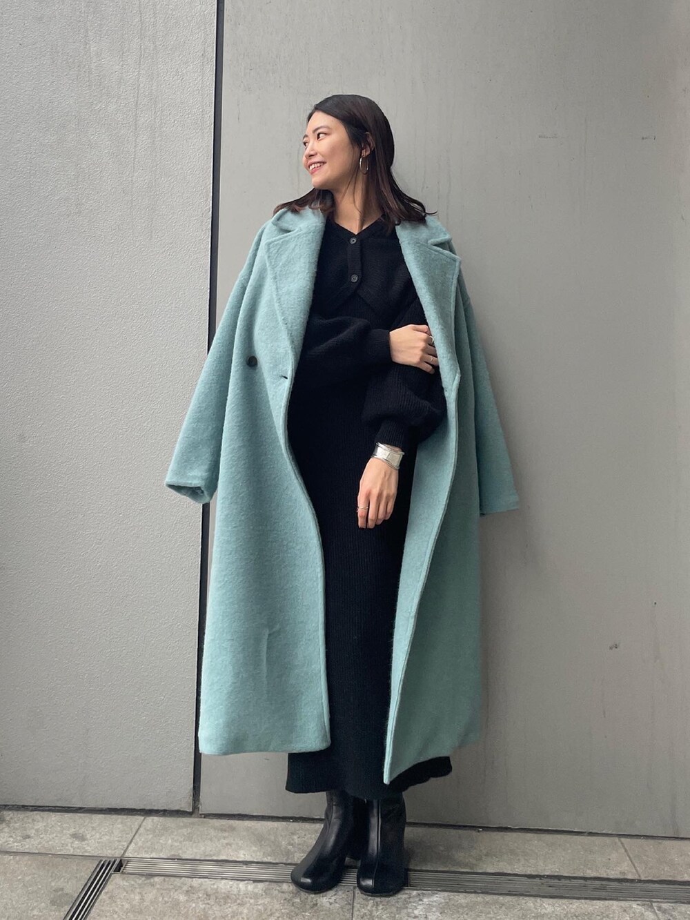 ブルー系のチェスターコート、ブラック系のワンピースを着用したレディースの冬コーディネートの2枚目の写真