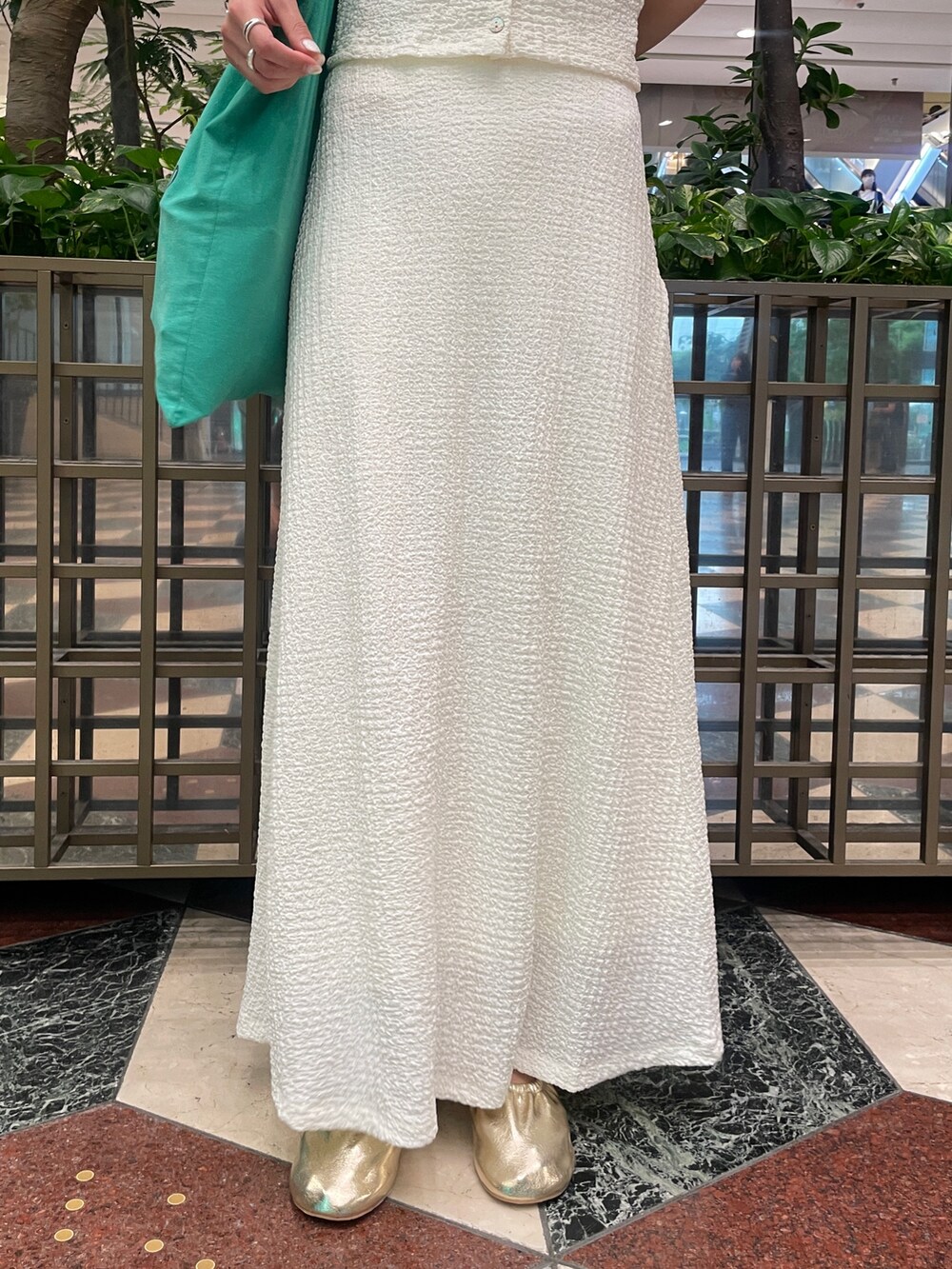 ホワイト系のスカート、ホワイト系のポロシャツ、ゴールド系のバレエシューズを着用したレディースの夏コーディネートの4枚目の写真