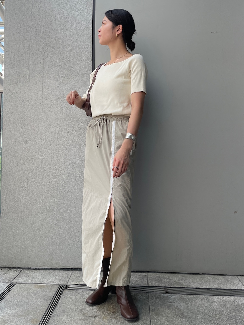 ベージュ系のスカート、ホワイト系のTシャツ/カットソー、ブラウン系のブーツを着用したレディースの夏コーディネートの2枚目の写真