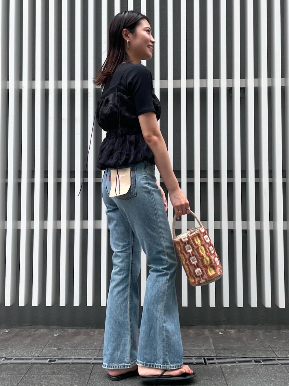 ブルー系のデニムパンツ、ブラック系のTシャツ/カットソー、ベージュ系のハンドバッグを着用したレディースの夏コーディネートの2枚目の写真