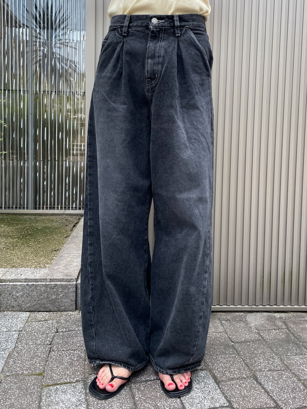 イエロー系のタンクトップ、ブラック系のデニムパンツ、ブラック系のサンダルを着用したレディースの夏コーディネートの5枚目の写真