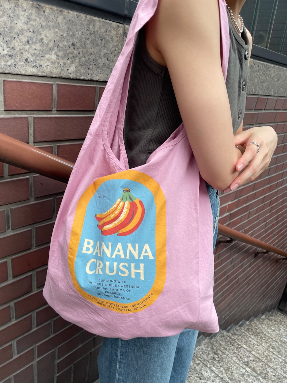 ピンク系のトートバッグ、ブルー系のデニムパンツ、グレー系のタンクトップを着用したレディースの夏コーディネートの4枚目の写真